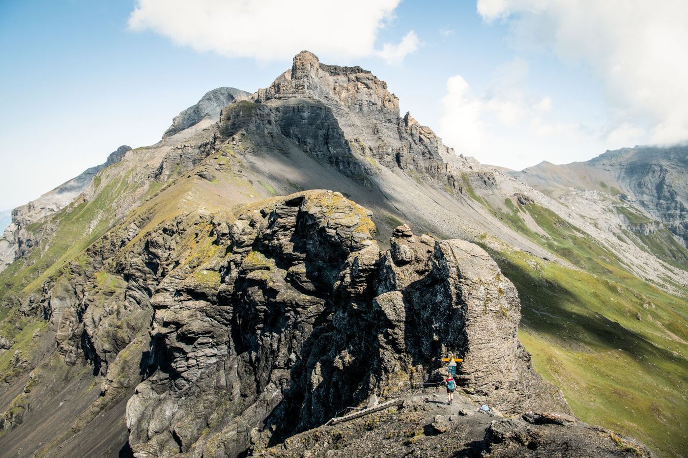 A hiker approaches a trail sign along a rocky ridge leading toward the imposing peak of the Hohtürli pass