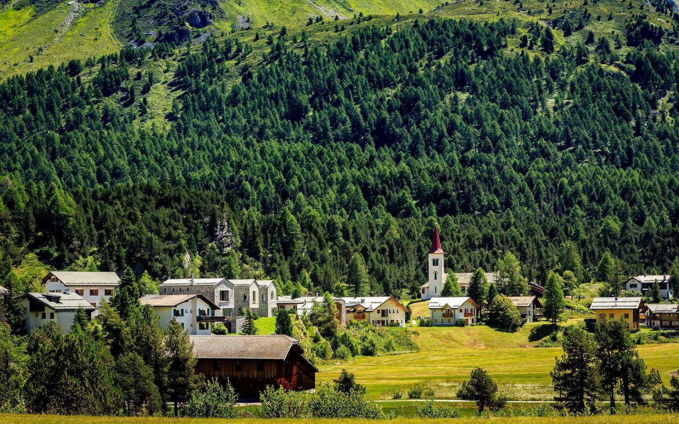 Alpine village of Maloja, Switzerland, showcasing traditional houses and a distinct red-roofed church