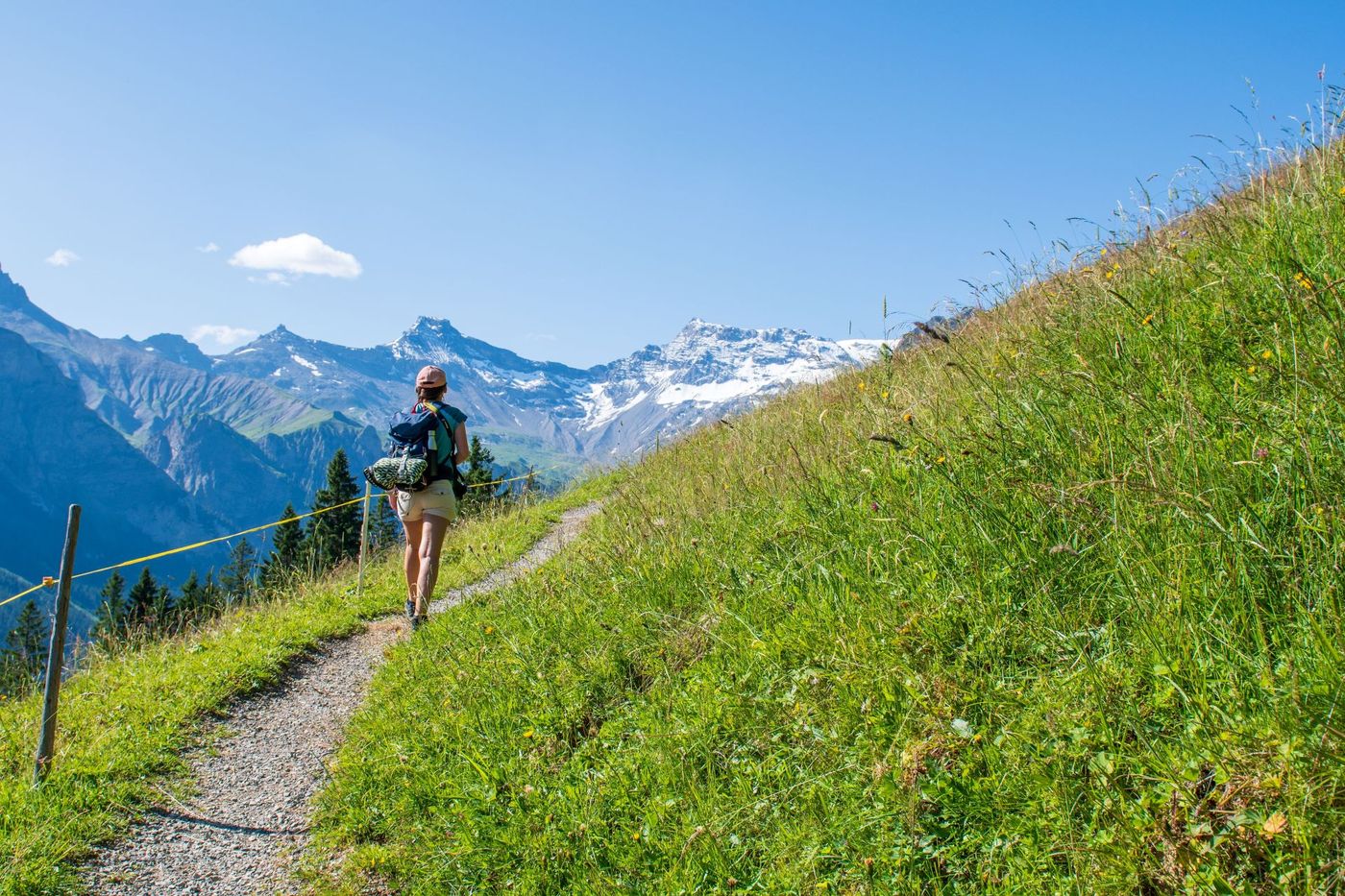 Hiker with a backpack walking along a narrow hiking in a hillside near Adelboden, Switzerland.